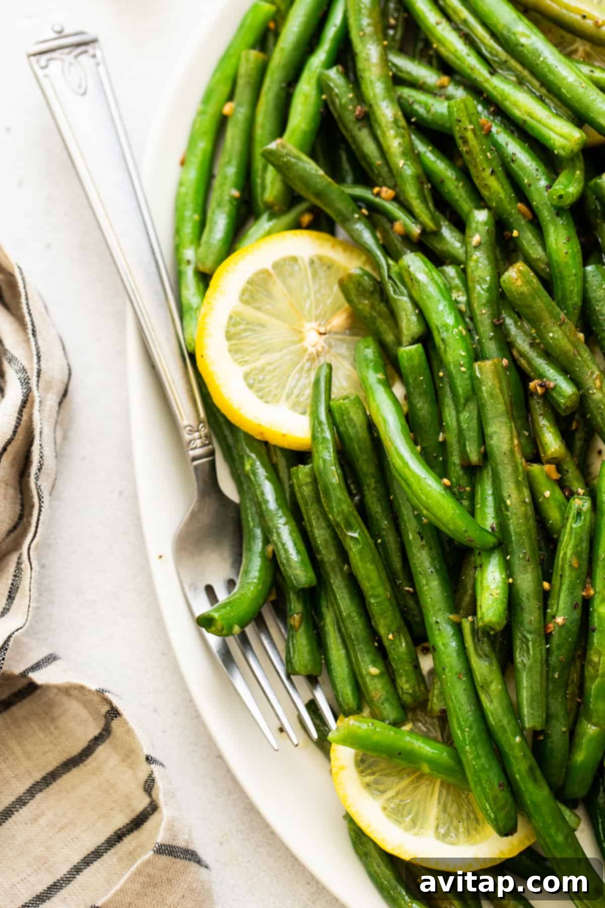 Cooked green beans with lemon and garlic on a platter Platter of perfectly cooked sautéed green beans, garnished with fresh lemon wedges and herbs.
