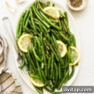Cooked green beans with lemon wedges on a platter.