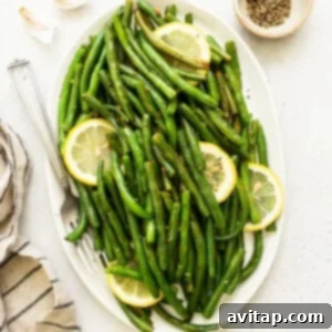 Platter of vibrant sautéed green beans with lemon wedges, ready to serve.