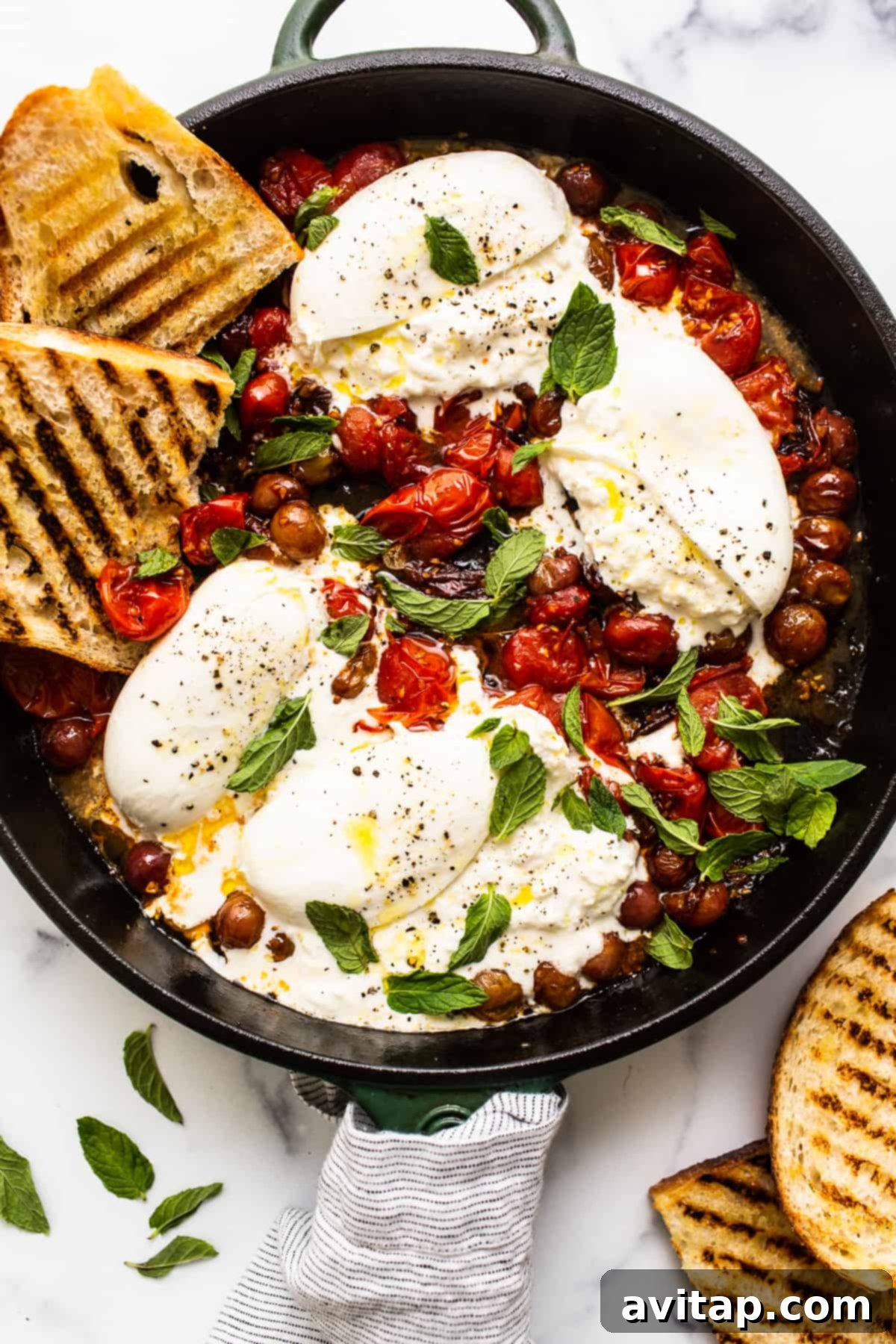 Delicious burrata appetizer served in a skillet, featuring roasted cherry tomatoes and grapes.