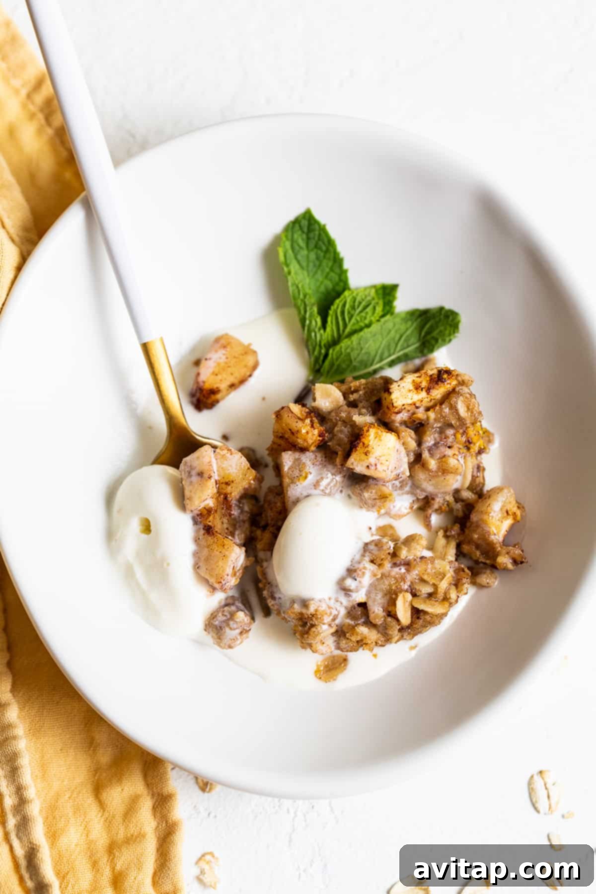 Mini apple crisp served in a bowl, generously topped with melting vanilla ice cream and a dusting of cinnamon.