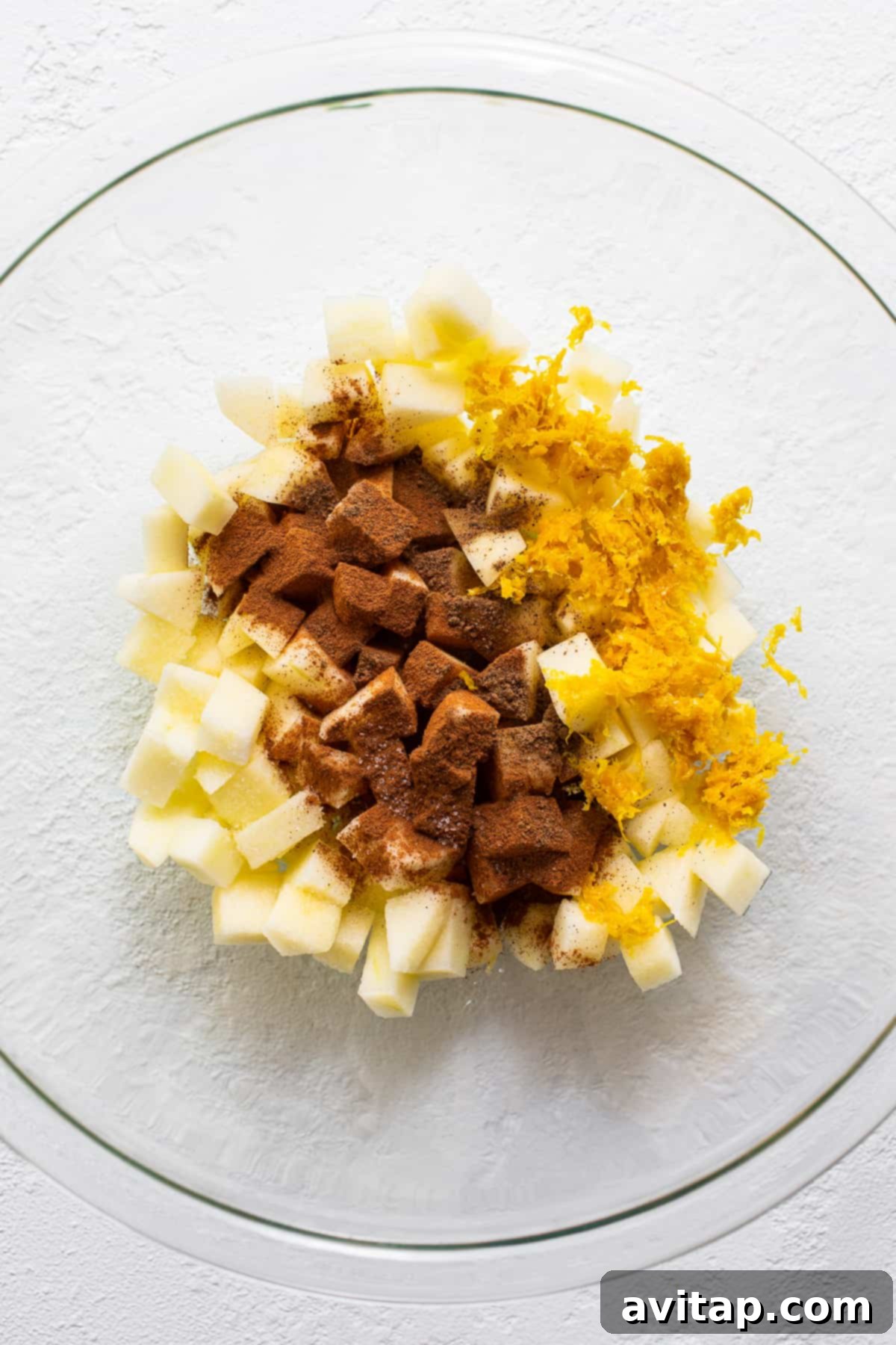 Close-up of a bowl filled with diced apples mixed with orange juice, zest, and spices, ready for the mini apple crisps.