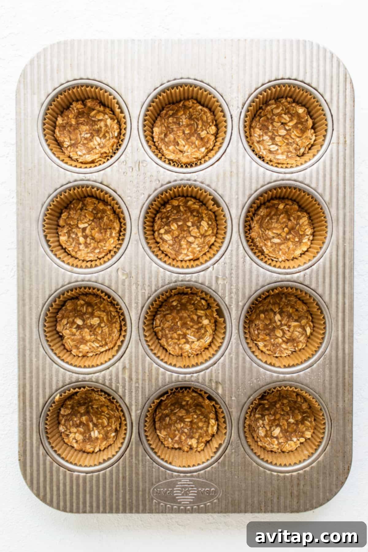 Muffin tin lined with paper cups, each containing a pressed apple crisp crust, ready for baking.