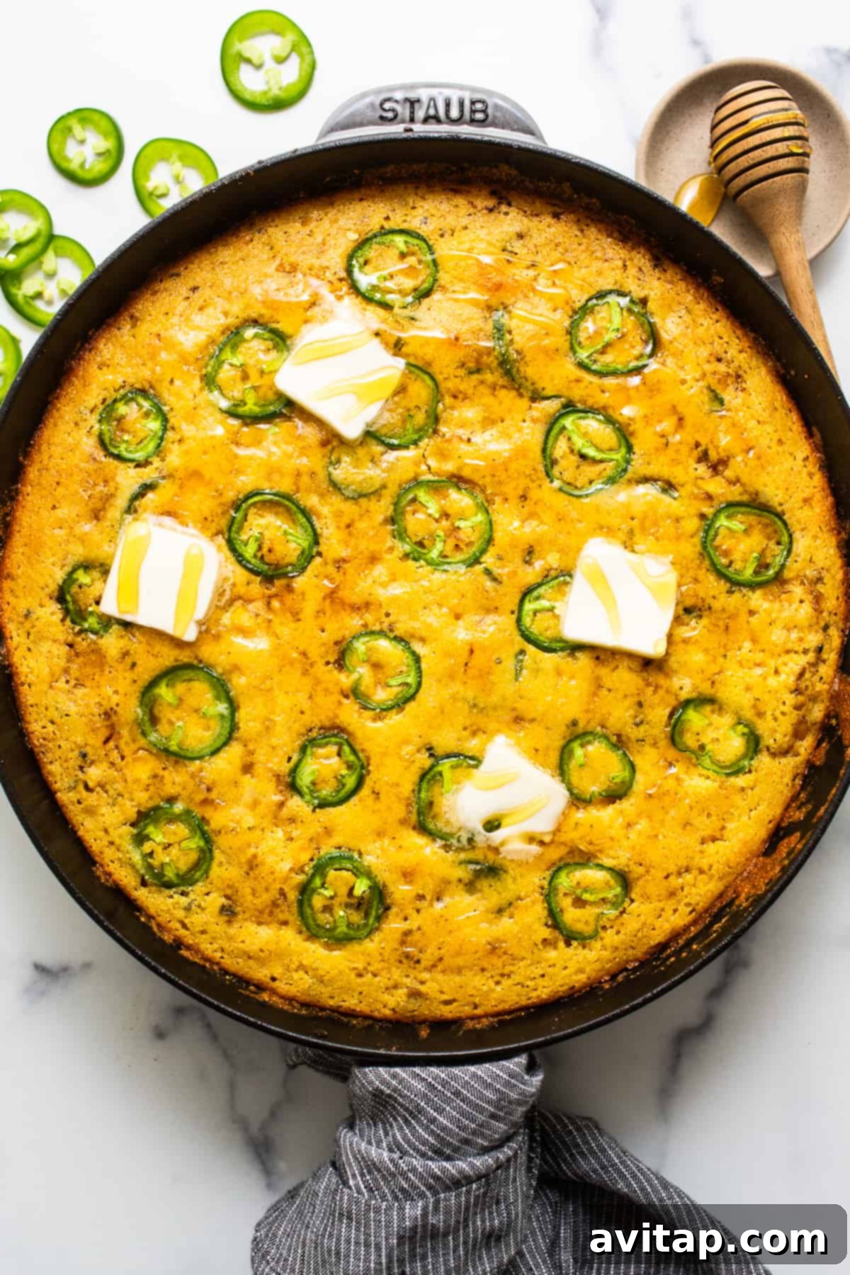 Golden brown jalapeño corn pudding in a cast iron skillet, topped with melting butter for extra richness. The pudding has a slightly bubbly, set texture.