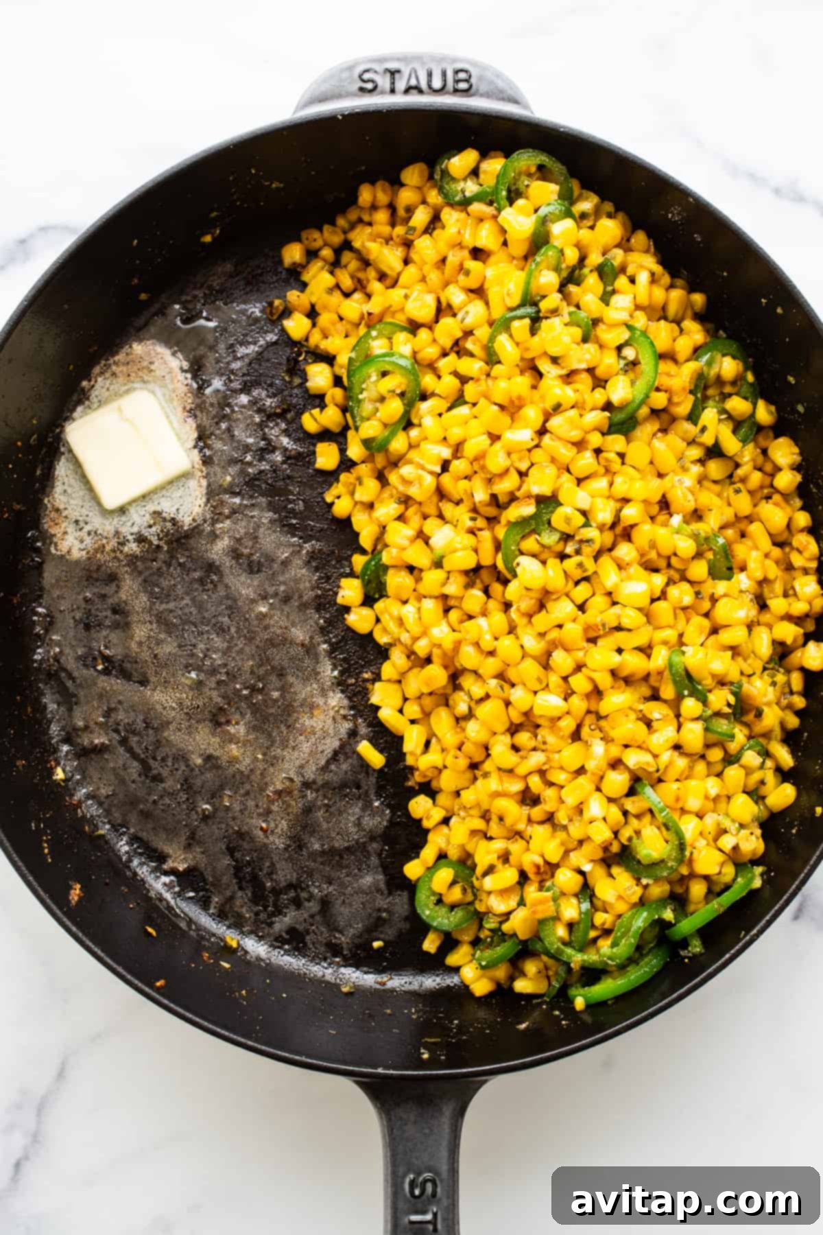 Fresh corn kernels and thinly sliced jalapeños simmering in a cast iron skillet with a pat of melting butter, illustrating the initial sautéing step.