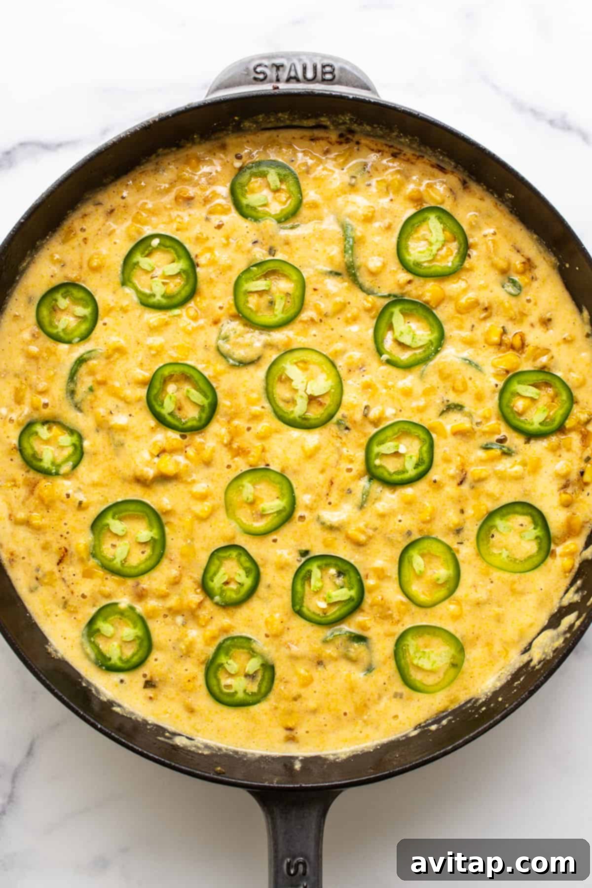 Jalapeño corn pudding in a cast iron skillet, beautifully golden and bubbling, ready for the oven with fresh jalapeño slices on top.
