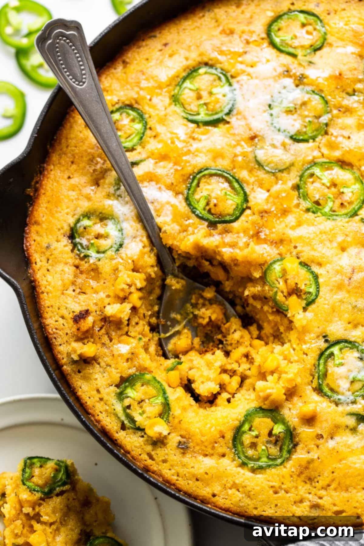 A serving spoon gracefully dipping into the warm, gooey, and flavorful center of the jalapeño corn pudding directly from the skillet, showcasing its soft texture.