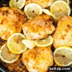 Seared chicken in a skillet with melting butter and fresh lemon slices.