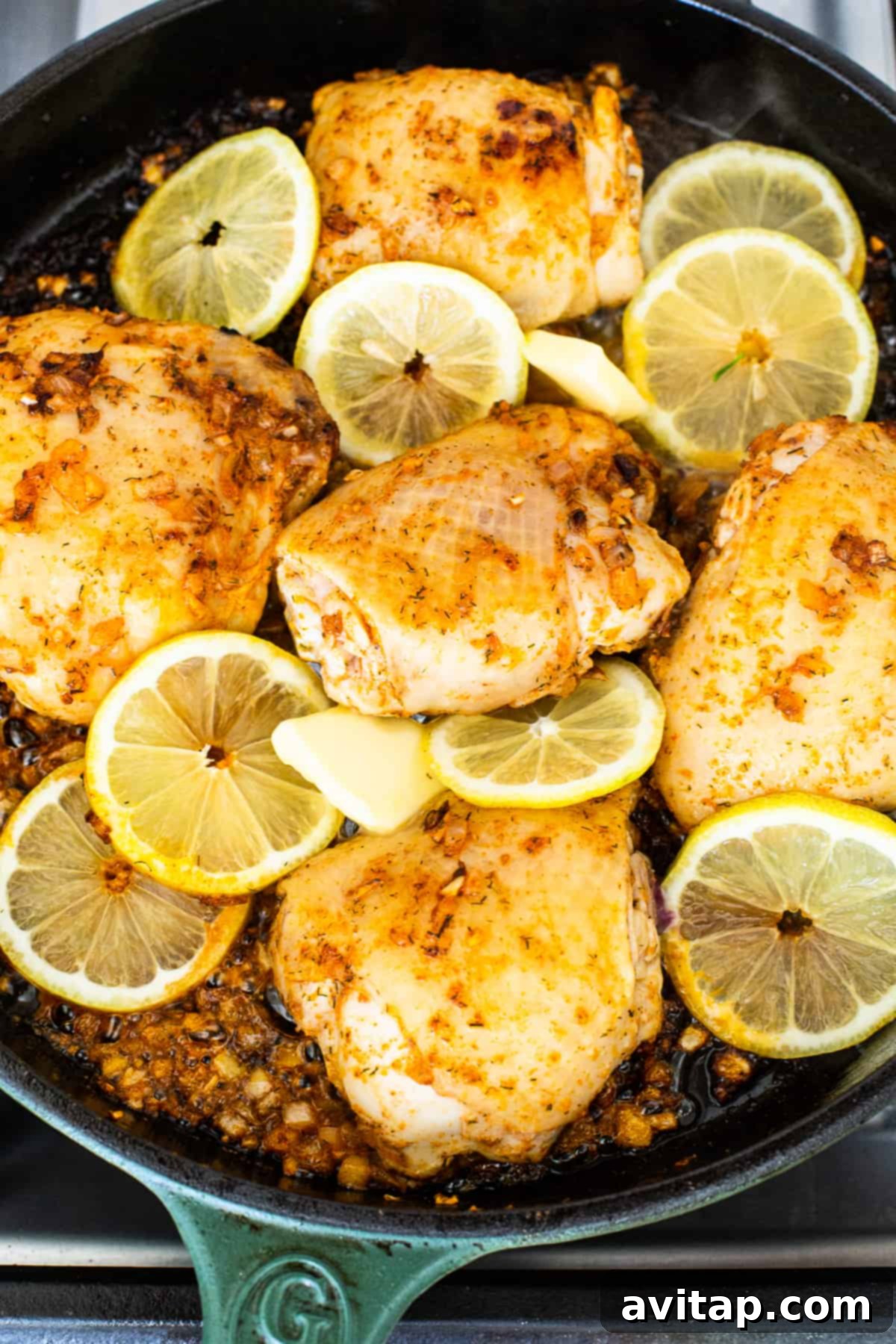Seared chicken thighs with lemon slices in a hot cast iron skillet.