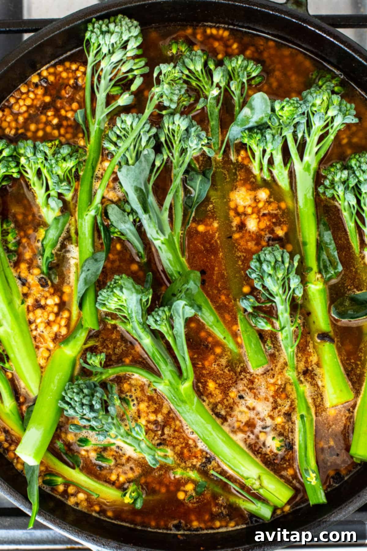 Fresh broccolini cooking in a cast iron skillet with liquid.