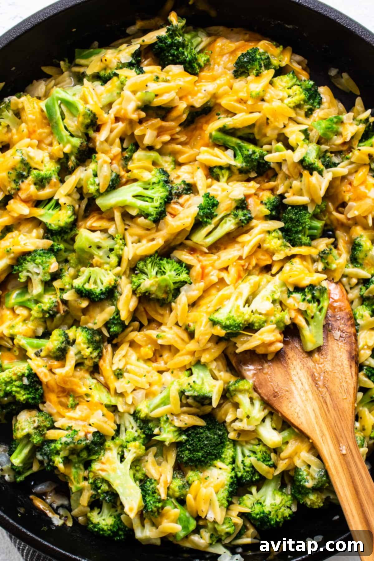Mixing the Cheesy Broccoli and Orzo Casserole A close-up of broccoli and cheese being mixed with orzo pasta in a cast iron skillet, showcasing the creamy texture.