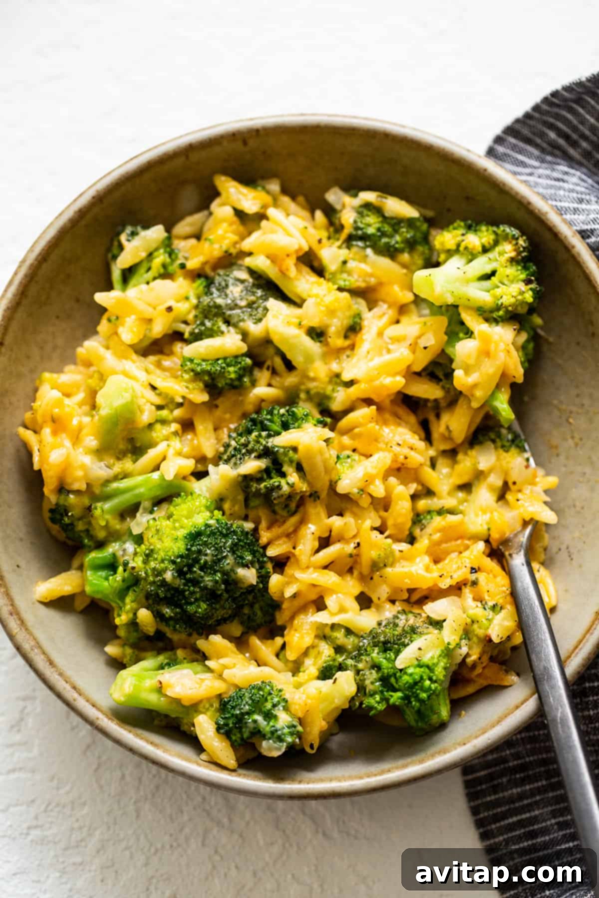 Broccoli Cheese Casserole with Orzo Served in a Bowl A serving of creamy broccoli and cheese casserole with orzo in a white bowl, ready to be enjoyed with a fork.