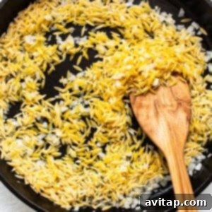 Orzo pasta being toasted in a cast iron skillet with onions and garlic, turning golden brown.