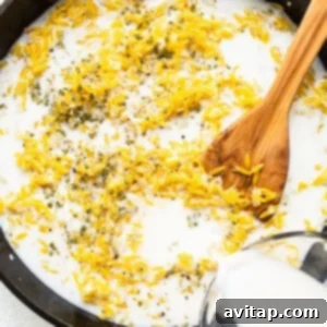 Pouring milk into a skillet containing toasted orzo and aromatics, preparing for simmering.