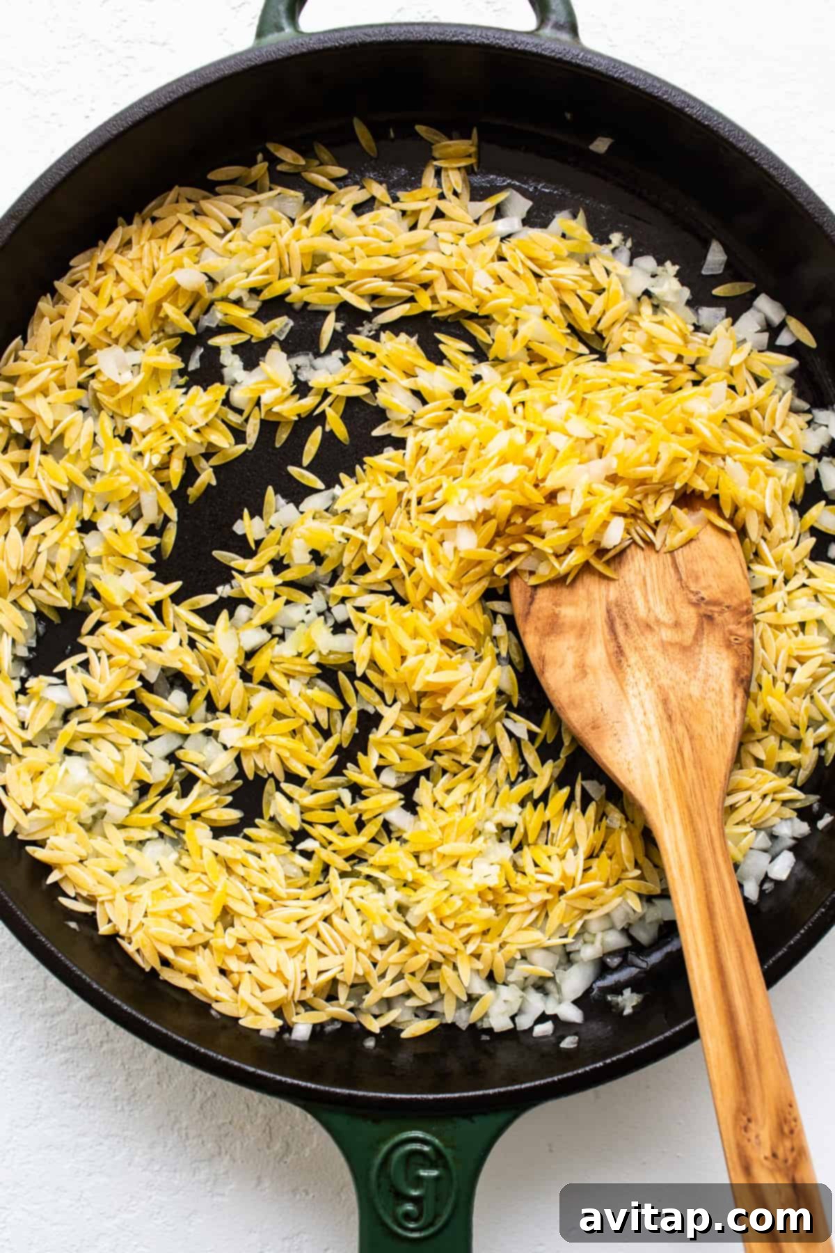 Toasting Orzo for the Ultimate Broccoli Cheese Casserole Golden orzo pasta being toasted to perfection in a cast iron skillet, giving it a delightful nutty flavor.