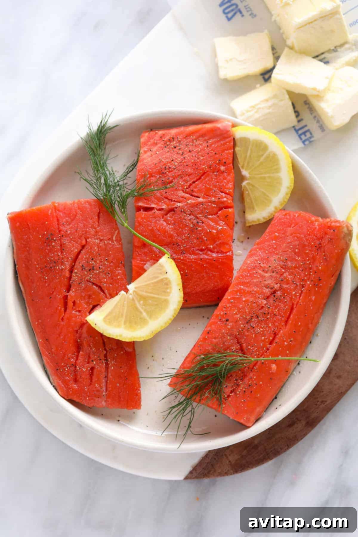 Make this Lemon Butter Pan Seared Salmon with 7 ingredients and in 30 minutes or less. This salmon is pan seared in a delicious lemon butter sauce leaving it so tender and flavorful. Uncooked salmon fillets with lemon slices and fresh dill on a plate, ready for searing.