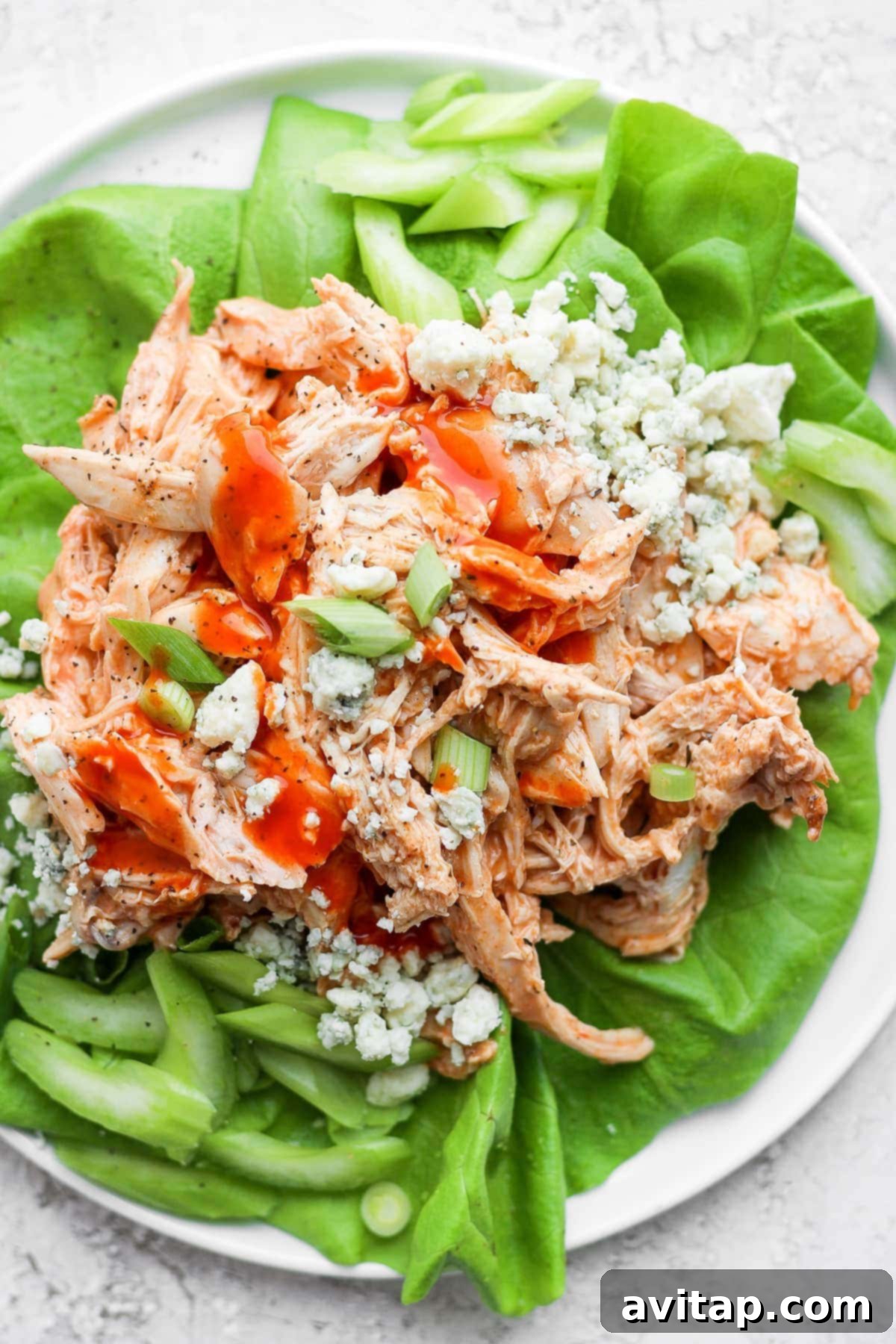 Shredded buffalo chicken in a crisp lettuce wrap, garnished with crumbled blue cheese, fresh celery sticks, and vibrant green onions for a healthy and flavorful meal.