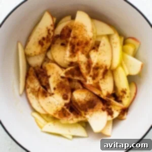 Apples marinating with spices and honey in a bowl.