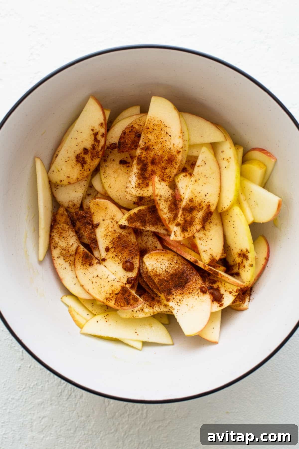 Sliced apples marinating with honey, chili powder, salt, and lemon juice in a mixing bowl.