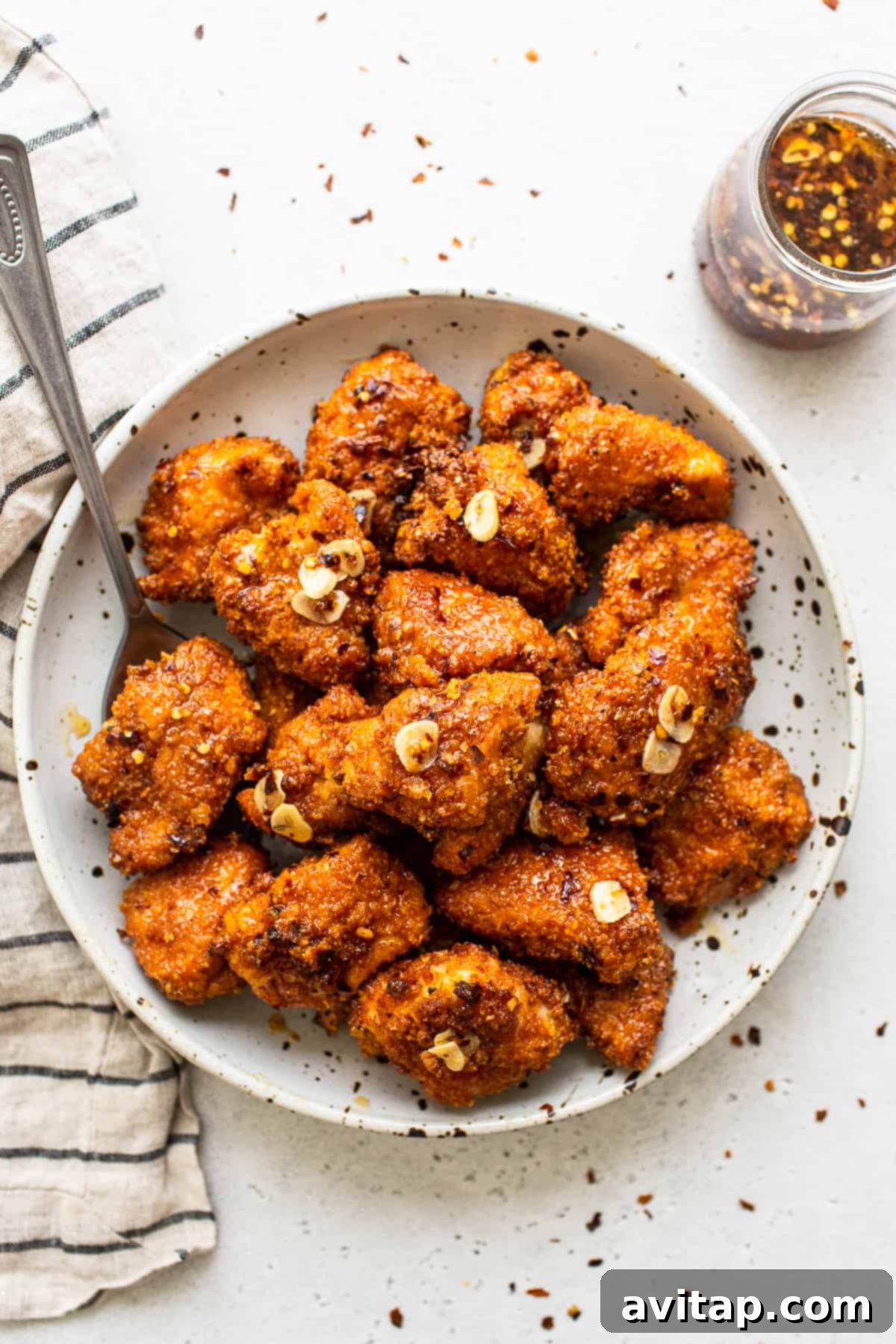A vibrant bowl of crispy Air Fryer Hot Honey Chicken with a spoon, ready to be enjoyed. The golden-brown chicken is coated in a glossy, spicy-sweet sauce.