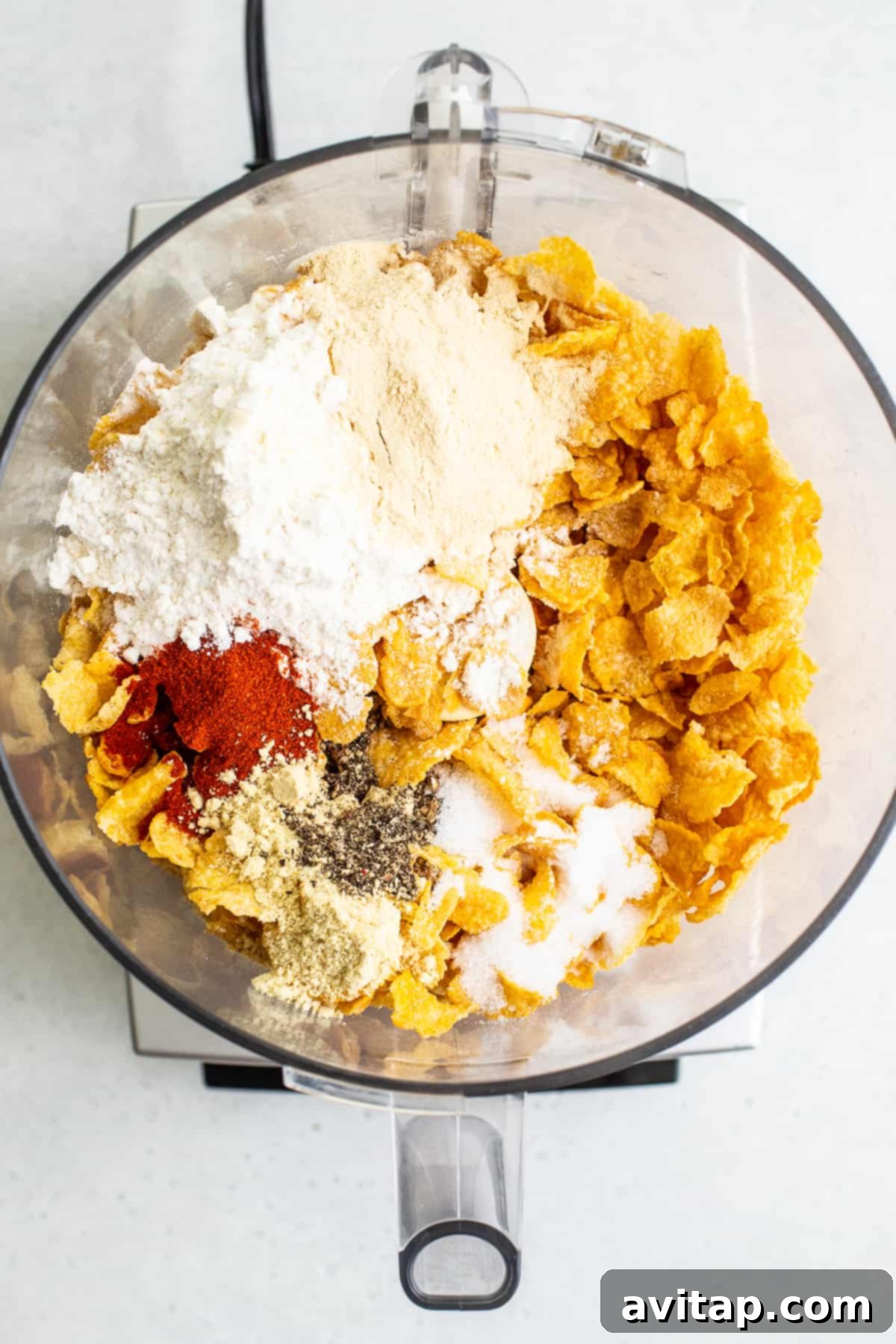 Close-up of cornflakes and an array of flavorful spices being processed in a food processor, creating the perfect crunchy coating for the chicken.