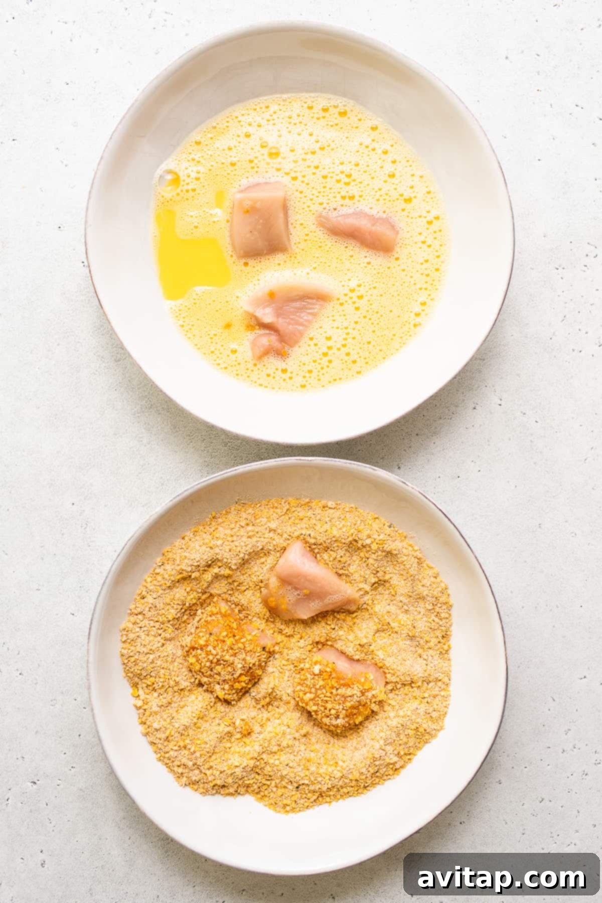 A hand dipping a piece of chicken into an egg wash bowl, showcasing the initial dredging process for the crispy coating.