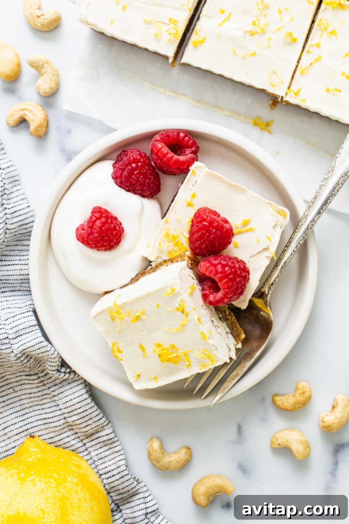 Effortless Vegan Cheesecake Bars 2 Exquisite lemon vegan cheesecake bars adorned with fresh raspberries and a sprinkle of cashews, elegantly presented on a white plate, highlighting their creamy texture and vibrant toppings.
