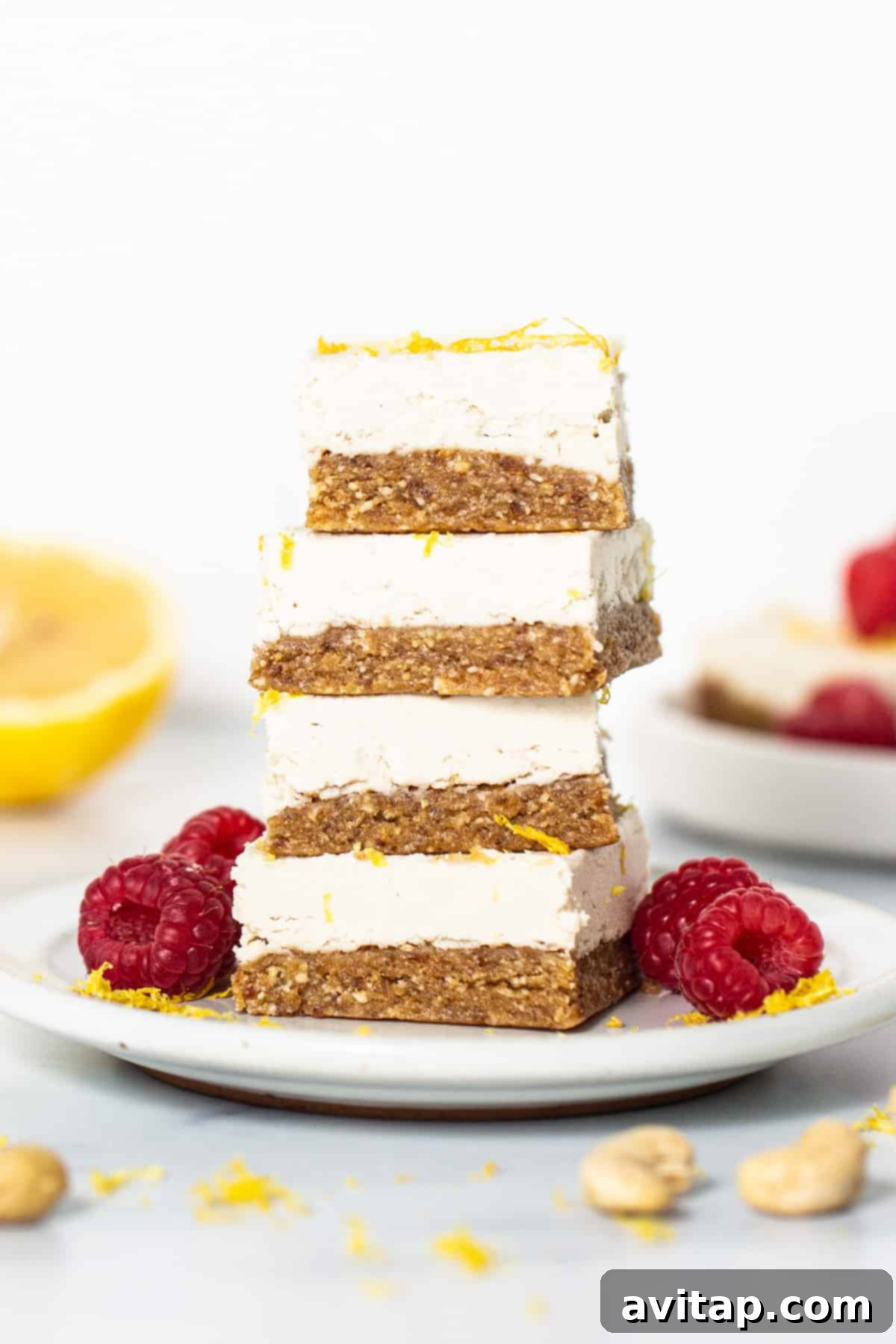 Effortless Vegan Cheesecake Bars 7 A beautifully arranged stack of lemon vegan cheesecake bars, generously garnished with fresh raspberries and a scattering of chopped nuts, ready for serving on a white plate.