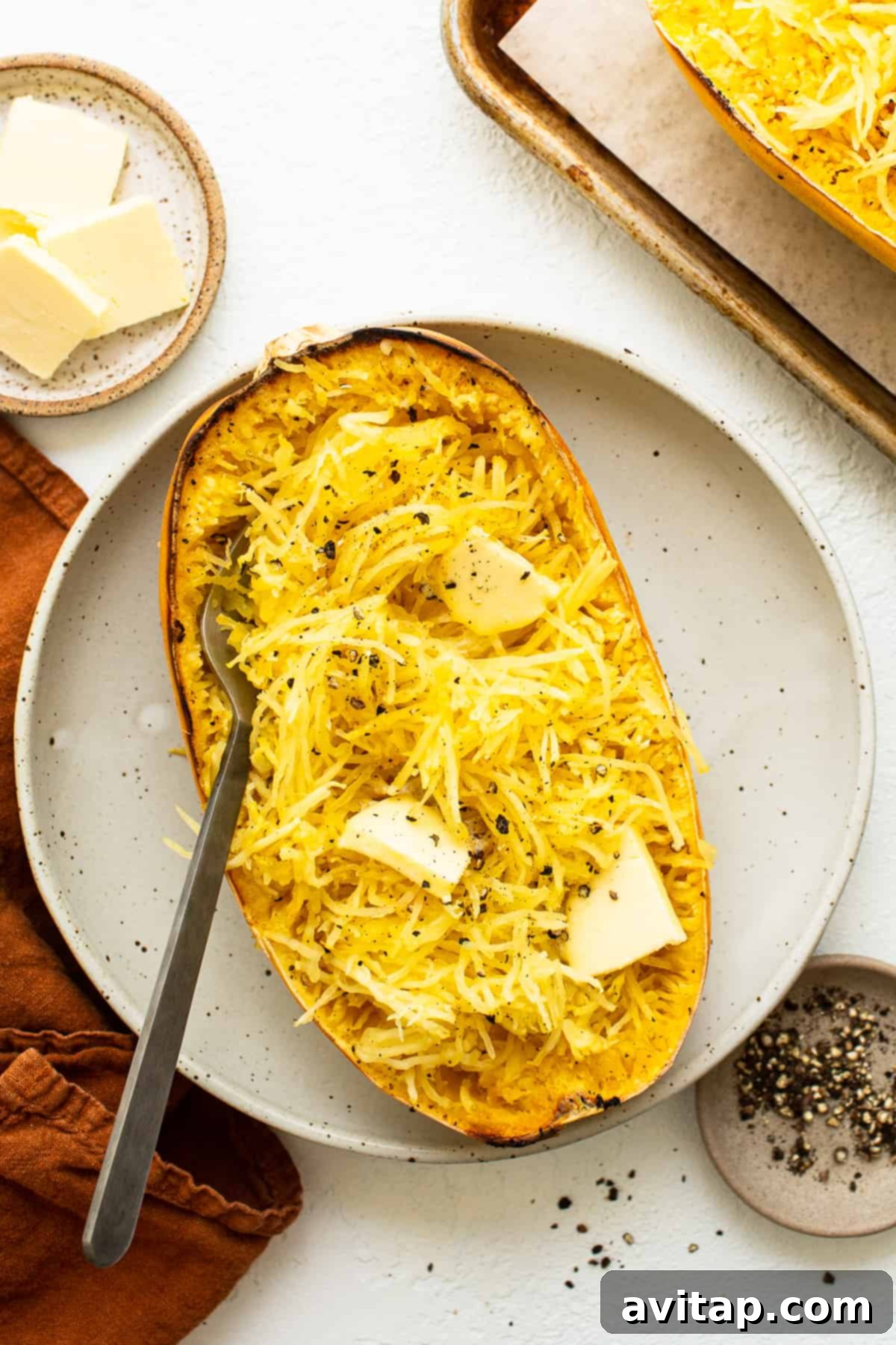 Golden baked spaghetti squash with melted butter and fresh herbs on a white plate, ready to be served.