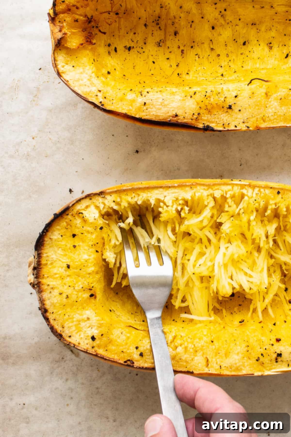 A fork carefully separating the golden, tender strands of baked spaghetti squash on a white plate, showcasing its pasta-like texture.