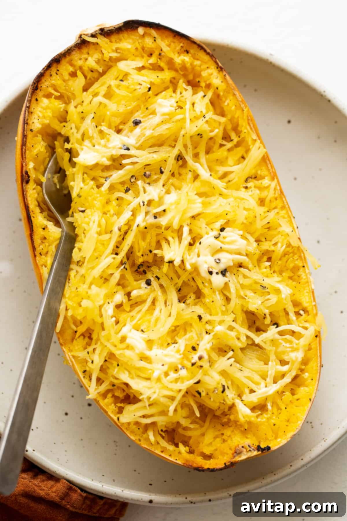 Close-up of baked spaghetti squash with a pat of butter melting on top and freshly cracked black pepper.