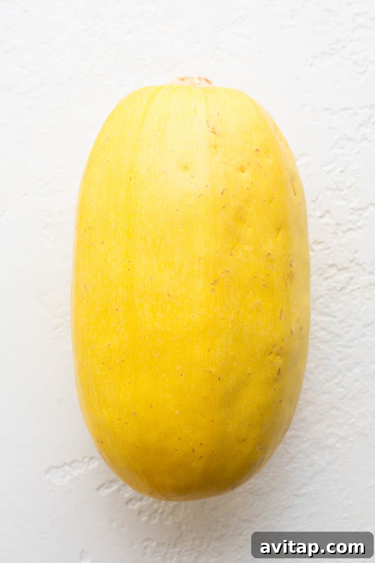 Two fresh, vibrant spaghetti squashes resting on a rustic wooden countertop, highlighting their readiness for cooking.