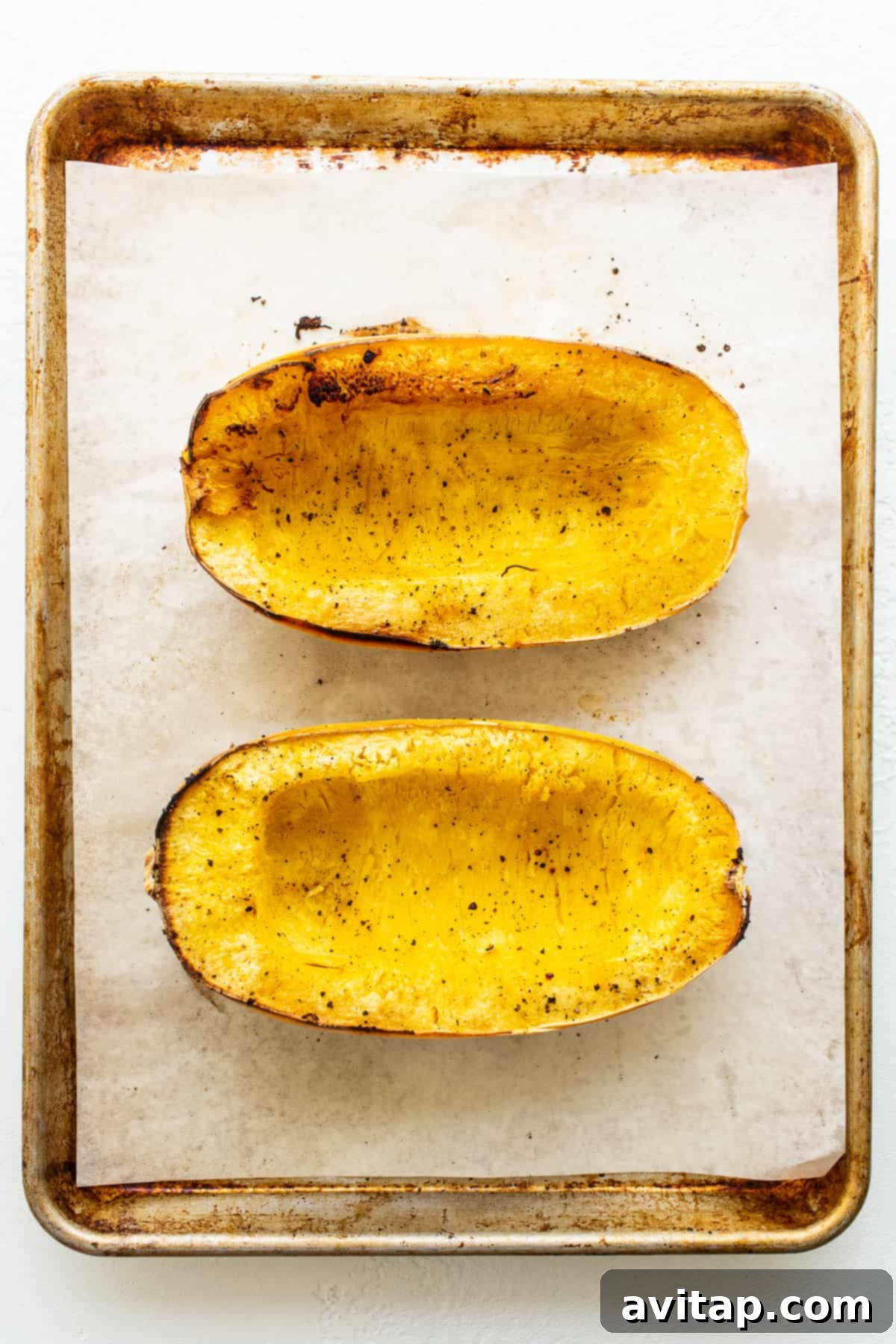 Freshly roasted spaghetti squash halves, golden brown and perfectly tender, cooling on a parchment-lined baking sheet.
