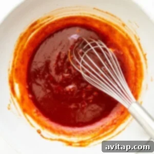 Weeknight Pork Noodles 4 A bowl of vibrant orange-red gochujang sauce, with a whisk, showing its smooth consistency.
