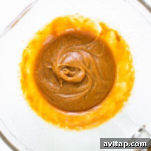 Peanut butter in a glass bowl mixed with wet ingredients for lactation cookies.