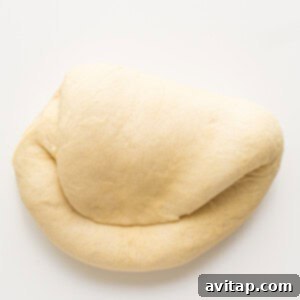 A smooth loaf of dough on a white surface, ready for its first rise.