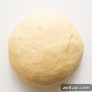 A ball of dough resting in a bowl, covered with plastic wrap, during its first rise.