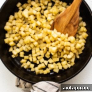 Diced apples sautéing in a skillet with a wooden spoon.