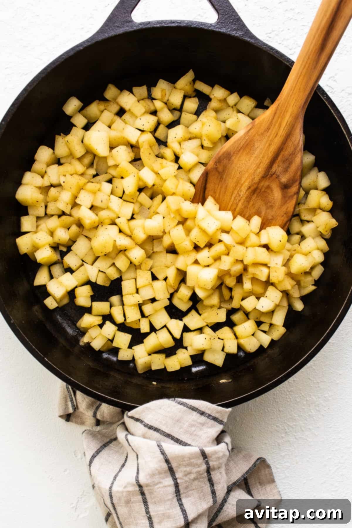 Diced Honeycrisp apples being sautéed in a cast iron skillet with butter and nutmeg, ready for the cinnamon roll filling.