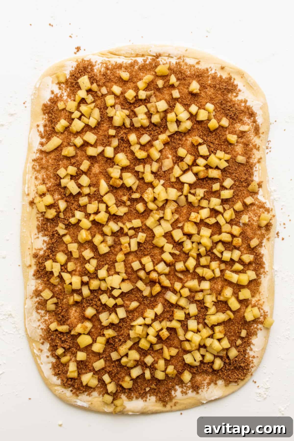 The apple cinnamon roll dough rolled into a rectangle, covered with the butter, brown sugar, and cinnamon filling, and sprinkled with diced sautéed apples.