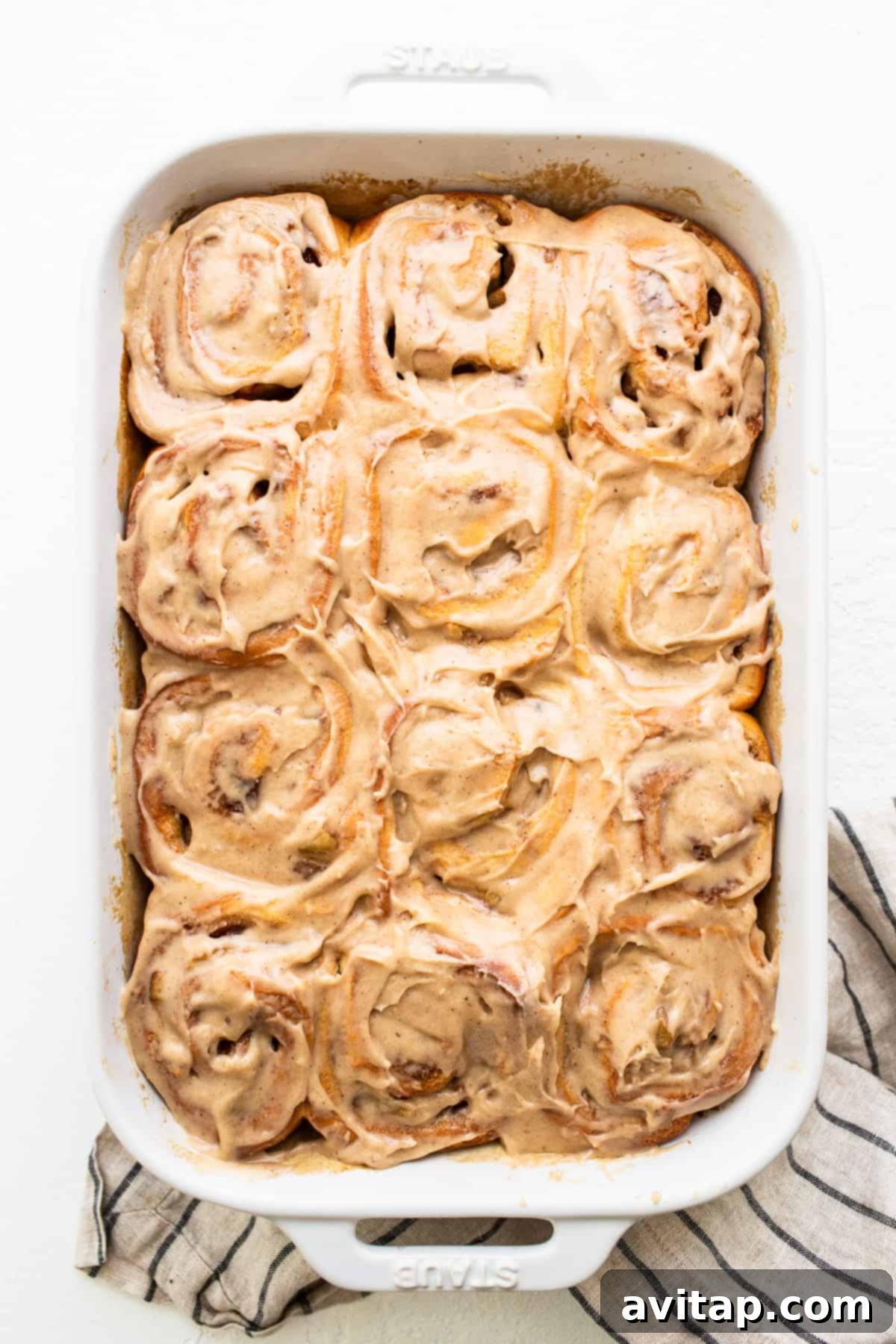 Close-up of baked apple cinnamon rolls, generously covered in creamy brown butter cream cheese frosting.