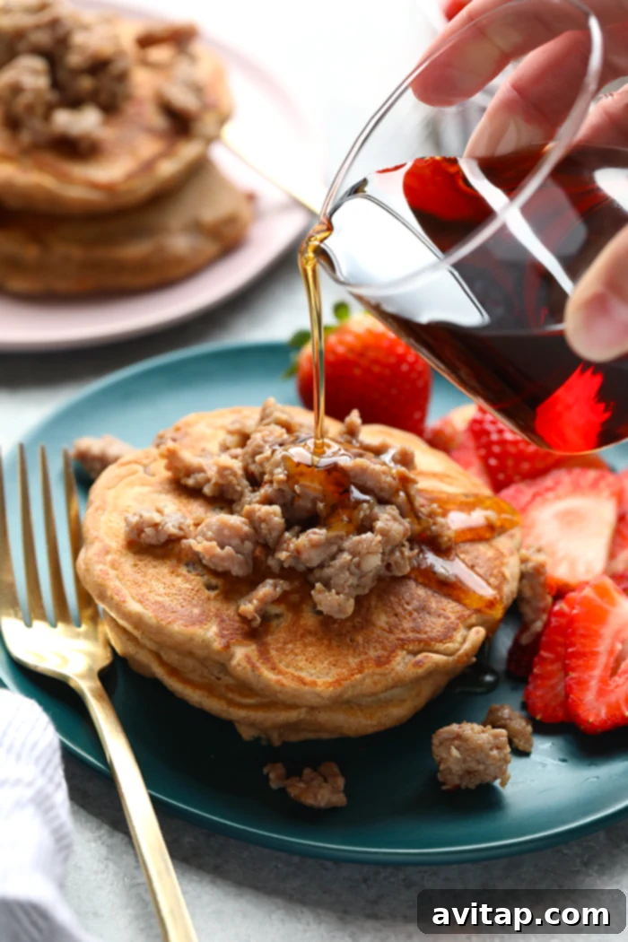 A stack of maple sausage pancakes, with sausage pieces embedded, drizzled with syrup and served on a rustic plate.