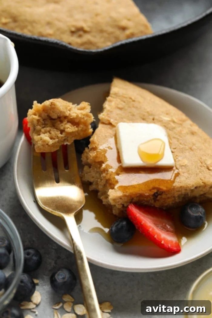 A large applesauce skillet pancake cake, baked golden brown, being drizzled generously with syrup, still in the skillet.