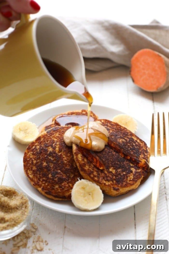 A stack of fluffy sweet potato power pancakes, garnished with pecans and syrup, served on a white plate.