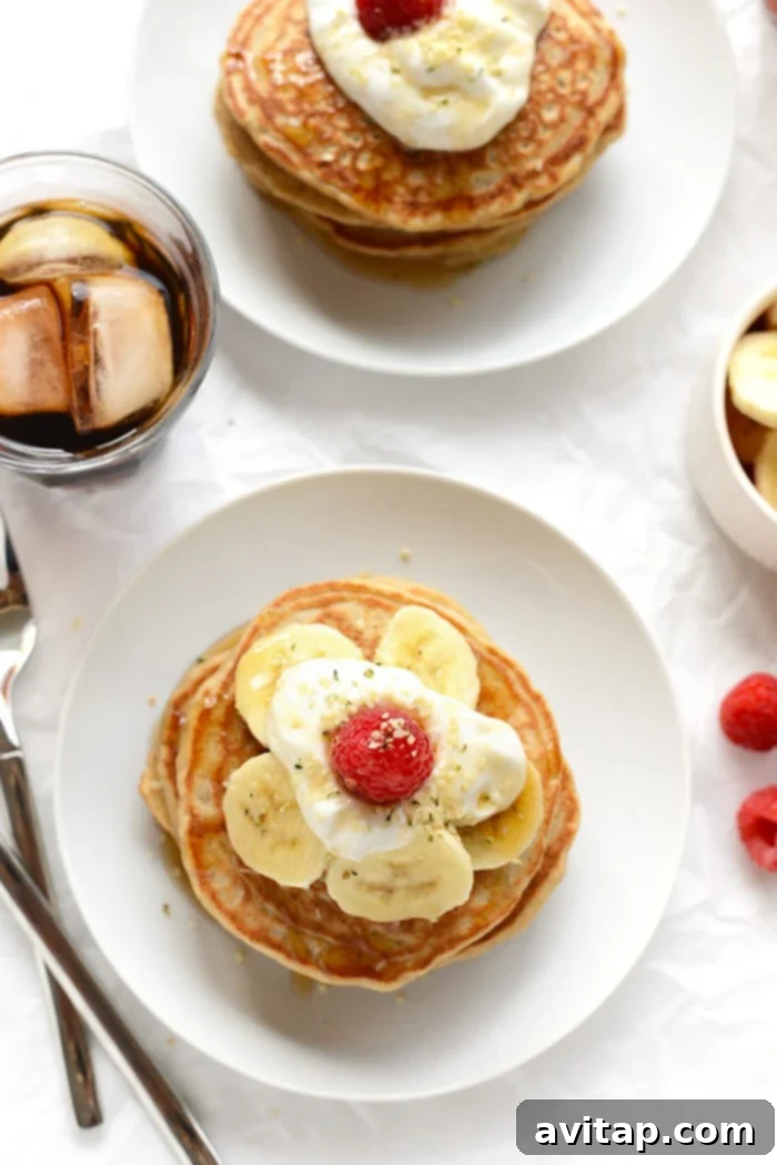 A stack of fluffy whole-grain banana pancakes, topped with fresh banana slices and berries, and a generous drizzle of syrup.