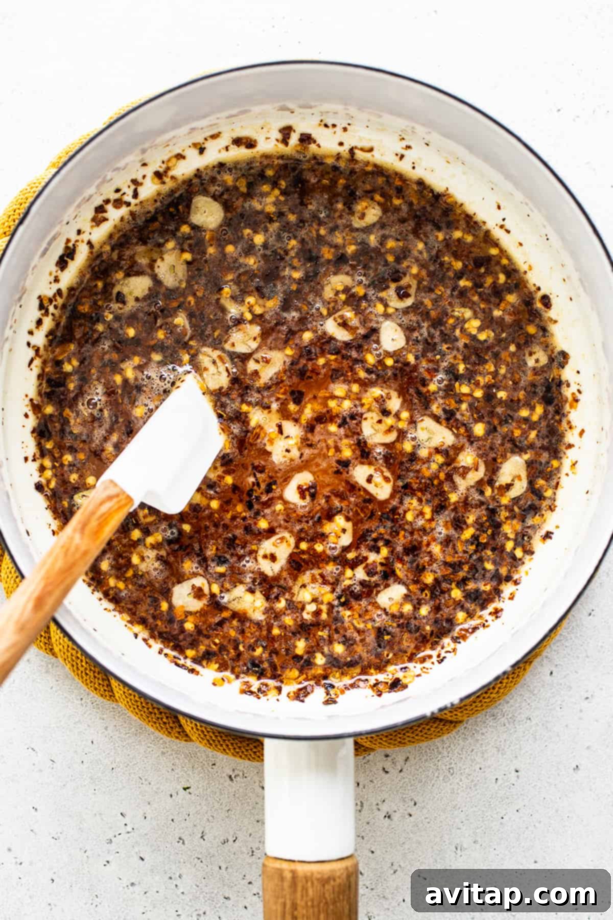 Hot honey mixture gently simmering in a small saucepan on a stove, with visible chili flakes and garlic slices infusing into the golden honey.
