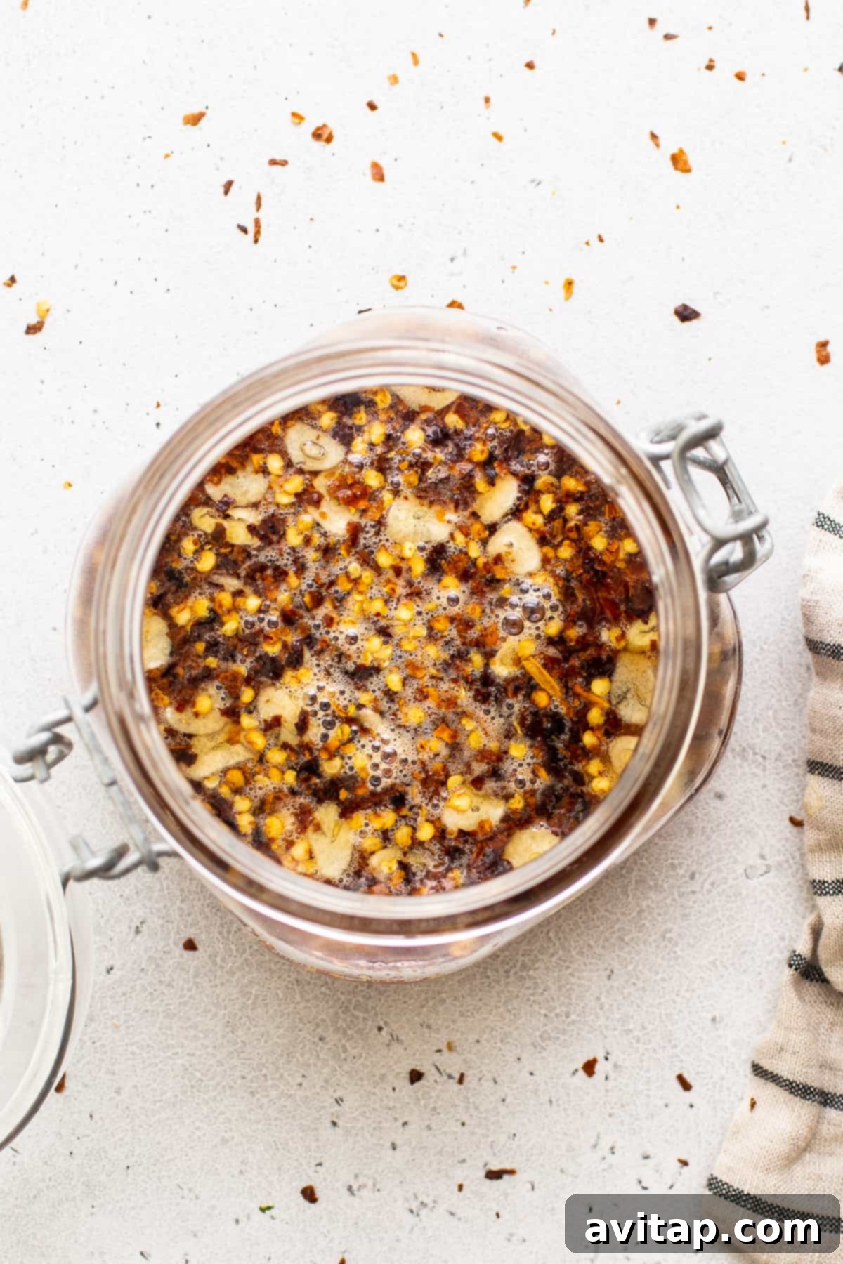 A rustic image of hot honey in a glass jar, perfectly showcasing its golden hue and the beautifully suspended chili flakes, against a textured background.