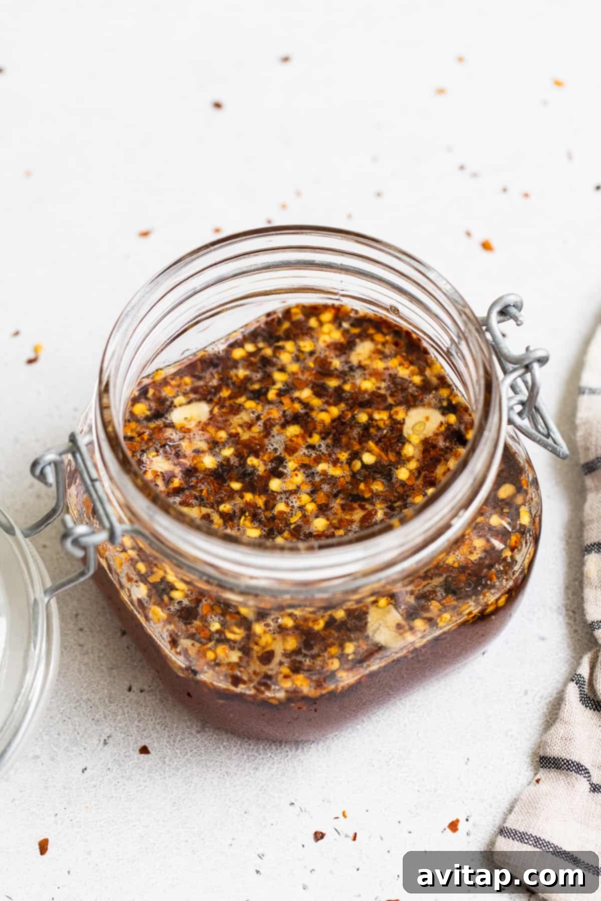 Hot honey sauce in a clear mason jar with visible chili flakes, beautifully presented on a wooden surface.