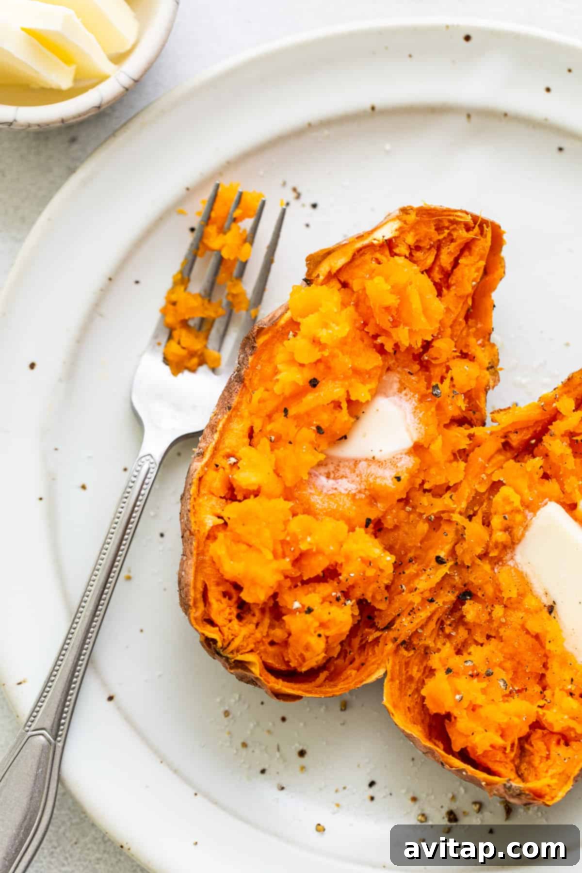 A perfectly cooked sweet potato on a plate, garnished with melted butter and freshly ground pepper, ready to eat.