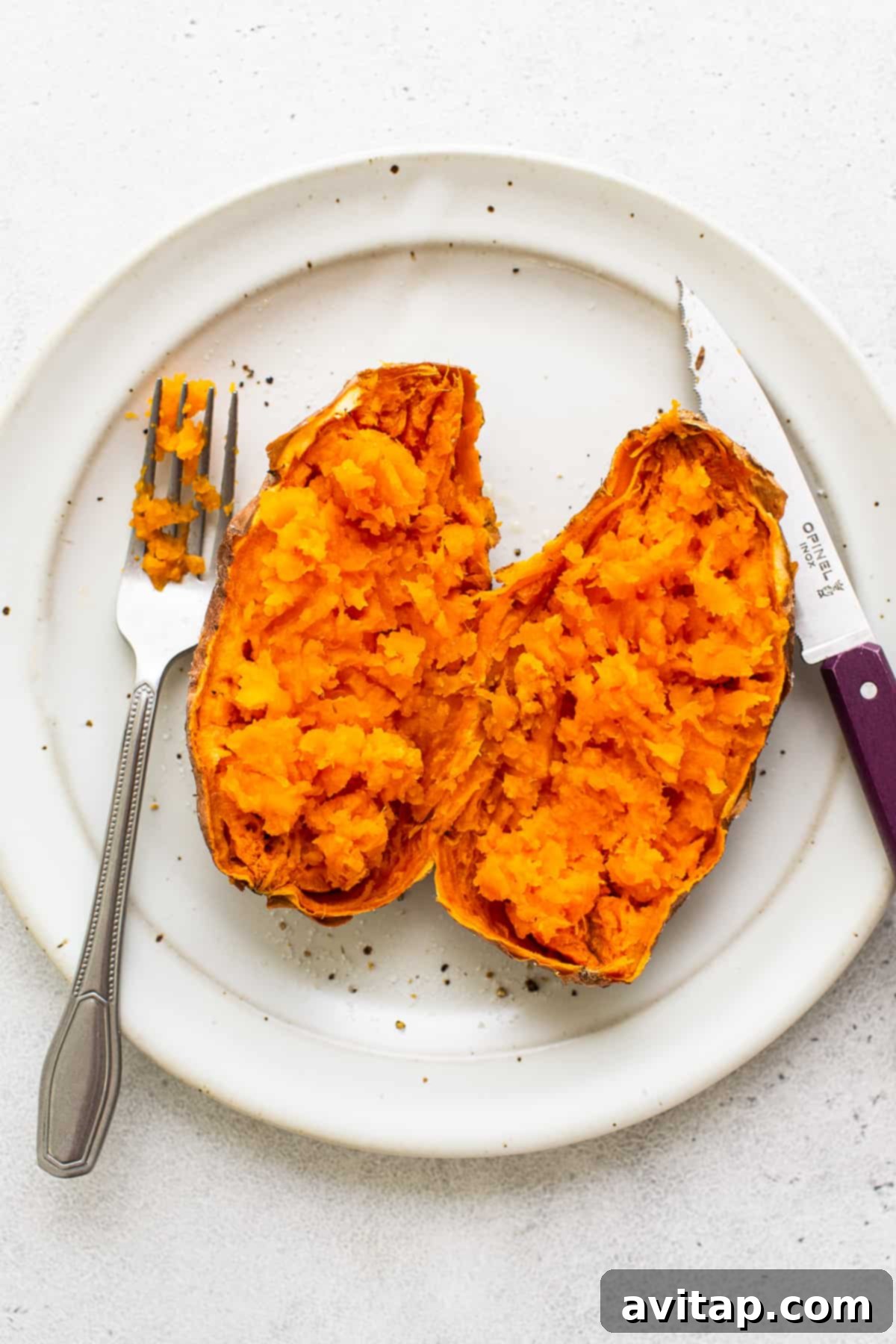 A sweet potato cut in half on a plate, with its fluffy interior exposed and ready for toppings. 